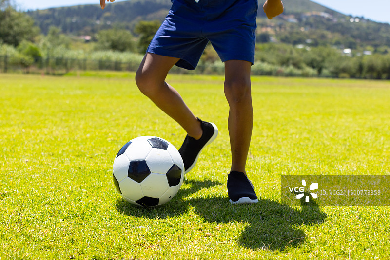 混血男孩在阳光明媚的场地上踢足球图片素材
