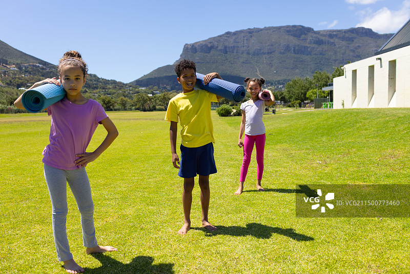 三个混血儿童站在草地上，带着瑜伽垫图片素材