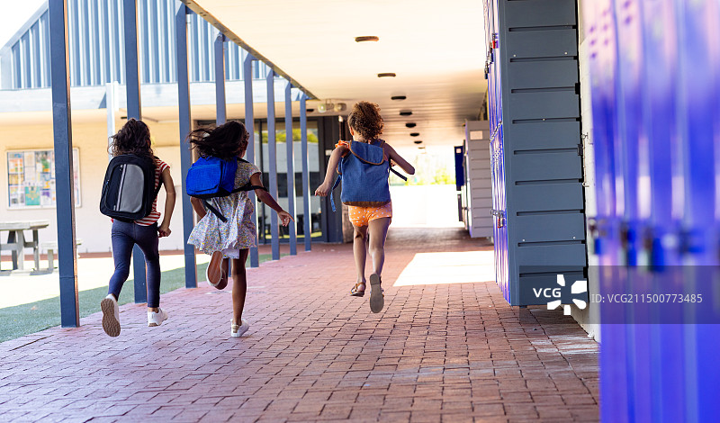 三个混血女孩背着书包跑过学校走廊图片素材