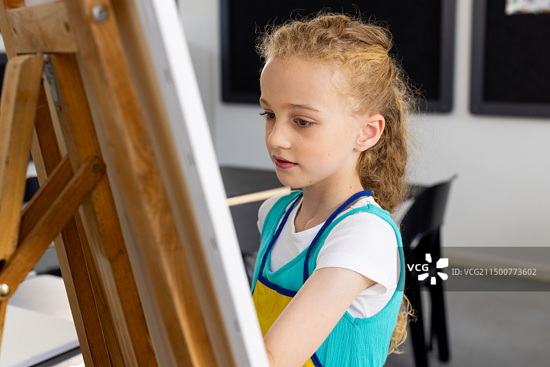 在学校的画架上绘画的卷发白人女孩图片素材