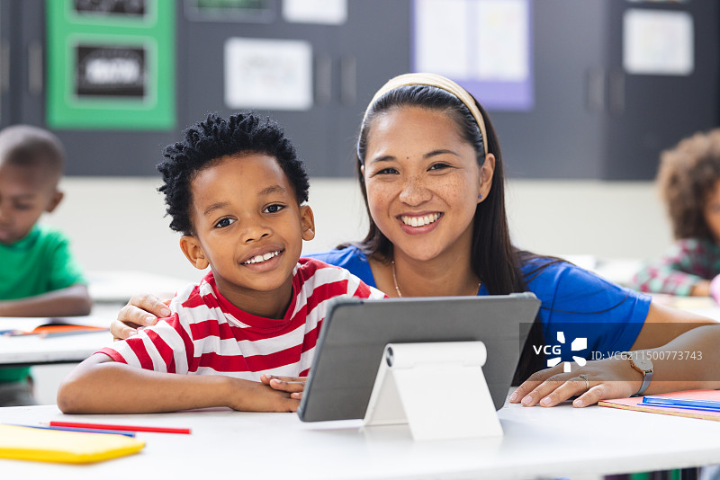 在教室里，一位混血老师和她的非裔美国孩子一起看平板电脑图片素材