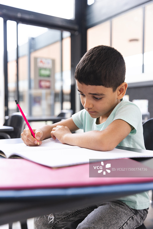 课堂上，混血男孩专注地在笔记本上写作图片素材