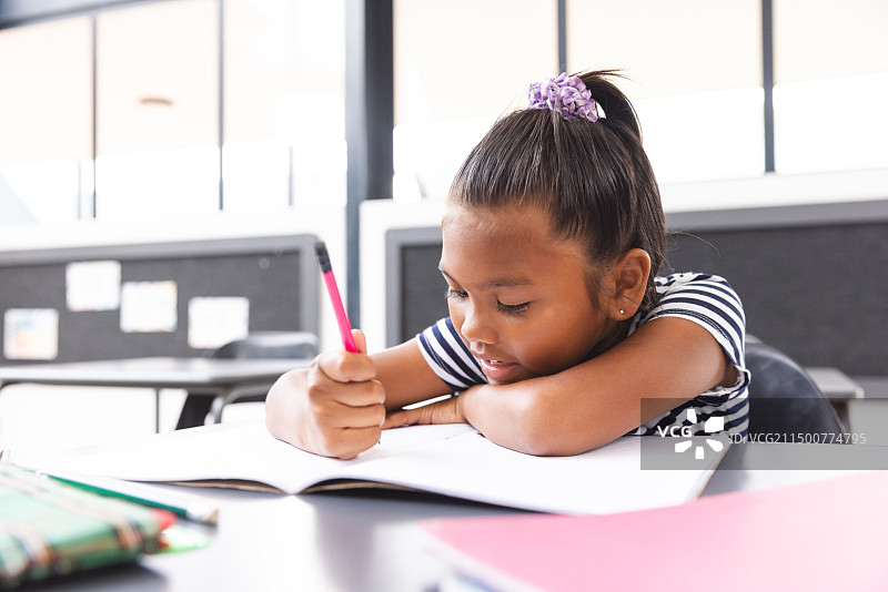 在学校教室里，一个年轻的混血女孩专心致志地在笔记本上写作图片素材