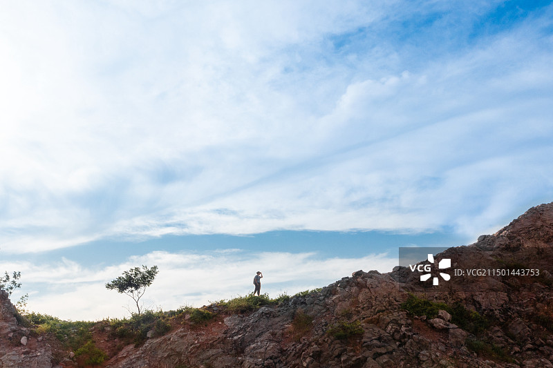 蓝天下远处有树的山脊上一个站立的人侧面图片素材