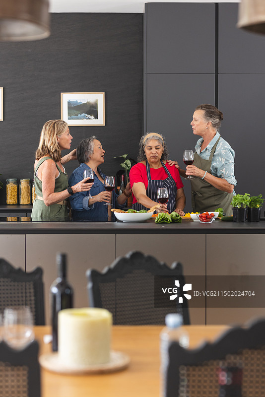 一群不同的女性在厨房里一起享受美酒和准备食物图片素材