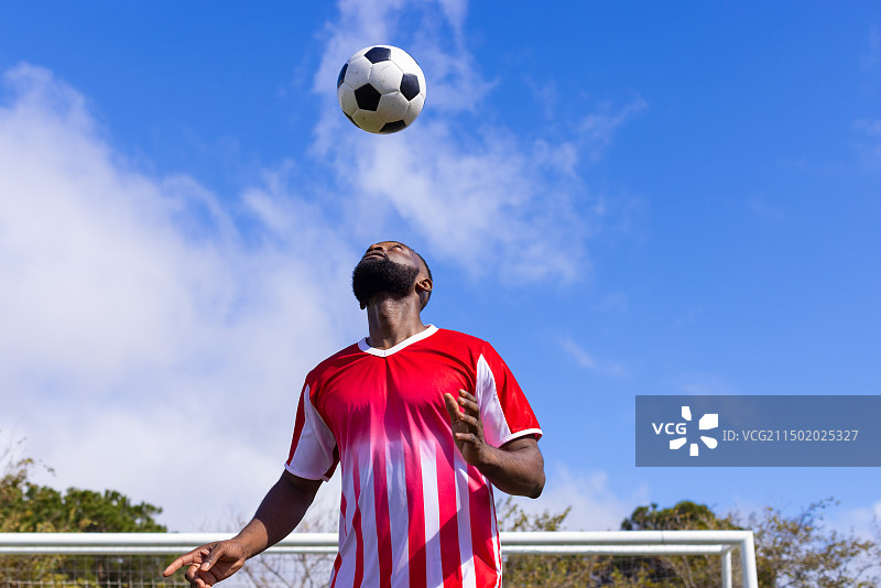 身穿红白球衣的非裔美国足球运动员用头平衡足球图片素材