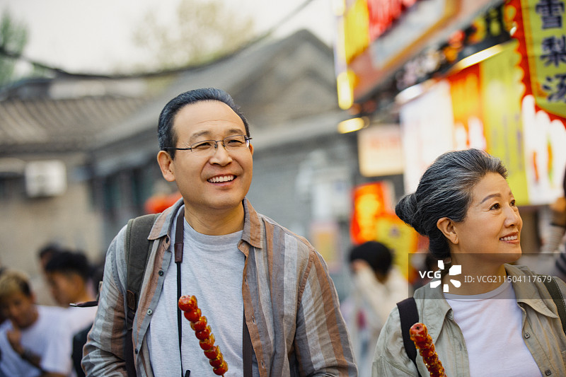 老年人City walk系列:老年夫妇拿着糖葫芦在北京胡同美食街旅行图片素材