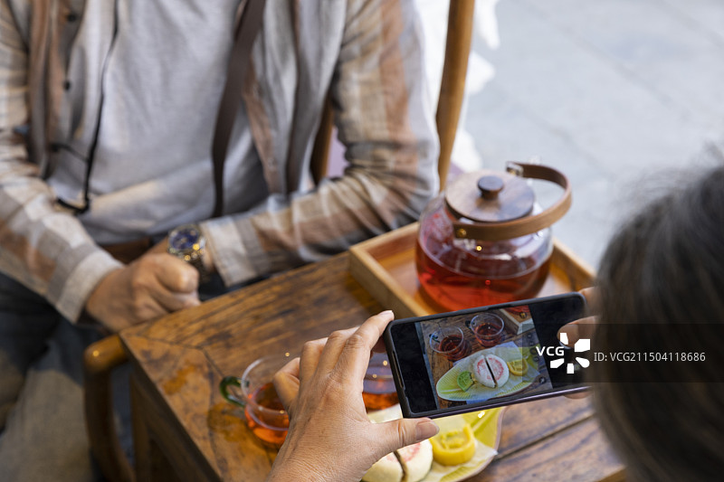 老年人City walk系列:老年夫妇用手机给中国茶和茶点拍照特写图片素材