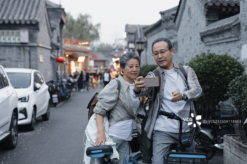 老年人City walk系列:老年夫妇在北京什刹海胡同骑共享单车合影自拍图片素材