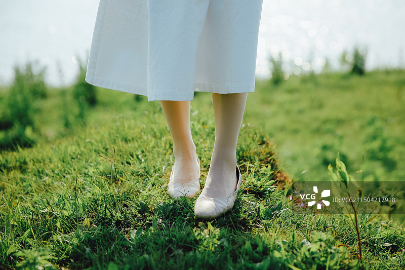 身穿白色裙子小白鞋的女孩双踩在草地上踏青图片素材