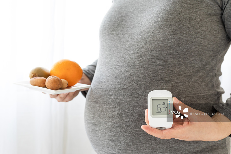 室内一名中国孕妇手拿着水果坚果和血糖仪图片素材