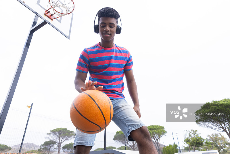 运球篮球，戴着耳机在球场上享受户外活动的青少年男孩图片素材