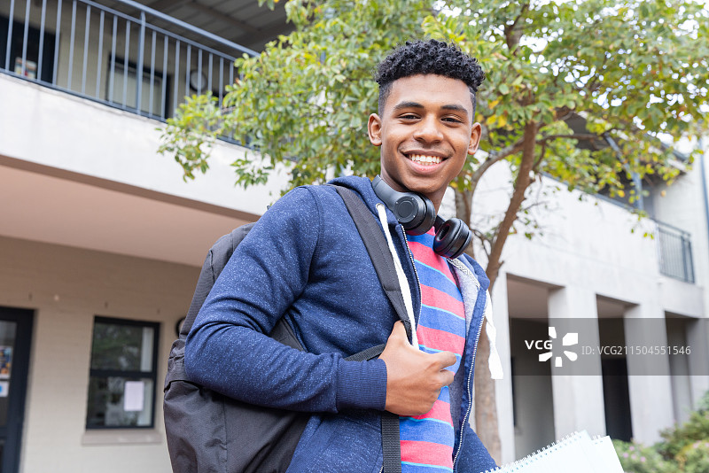 背着背包、戴着耳机站在教学楼外的微笑男学生图片素材