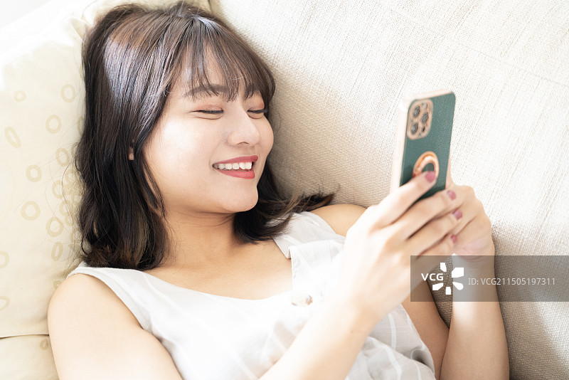 女人躺在沙发上看着手机微笑图片素材