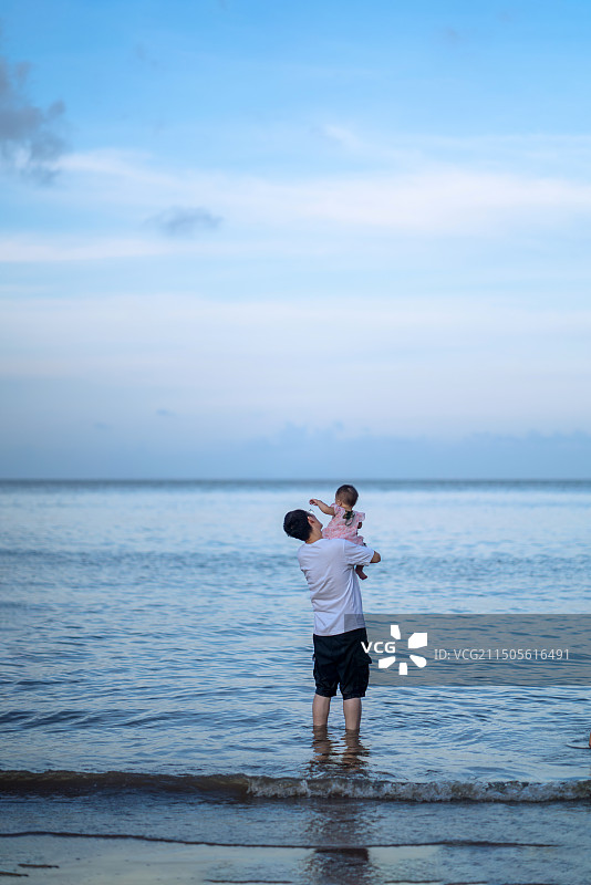父亲抱着女儿站在海边沙滩上的后视图图片素材