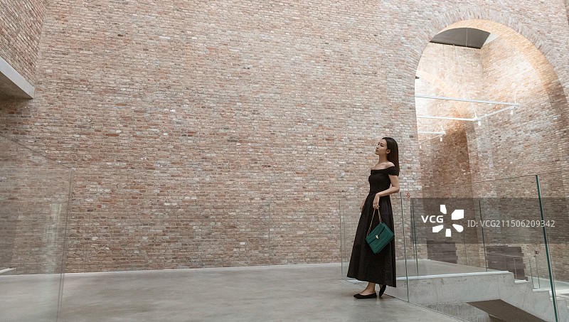 在艺术空间里站着的年轻女子 红色的砖墙图片素材