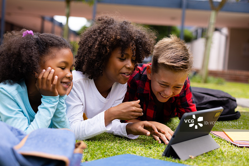 快乐的小学生们在学校草地上使用平板电脑图片素材
