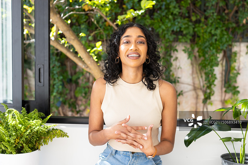 在室内与植物进行视频通话的微笑的女人，穿着休闲服装和珠宝图片素材