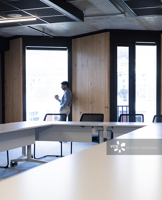 站在窗边的商务男士在现代办公室里手持咖啡杯，留白图片素材