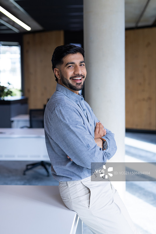 在办公室里双臂交叉靠在桌子上的微笑商人图片素材
