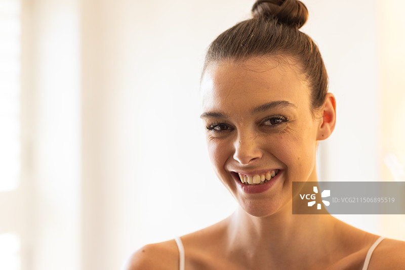 在家中，在自然光下看着镜头的微笑年轻女人图片素材