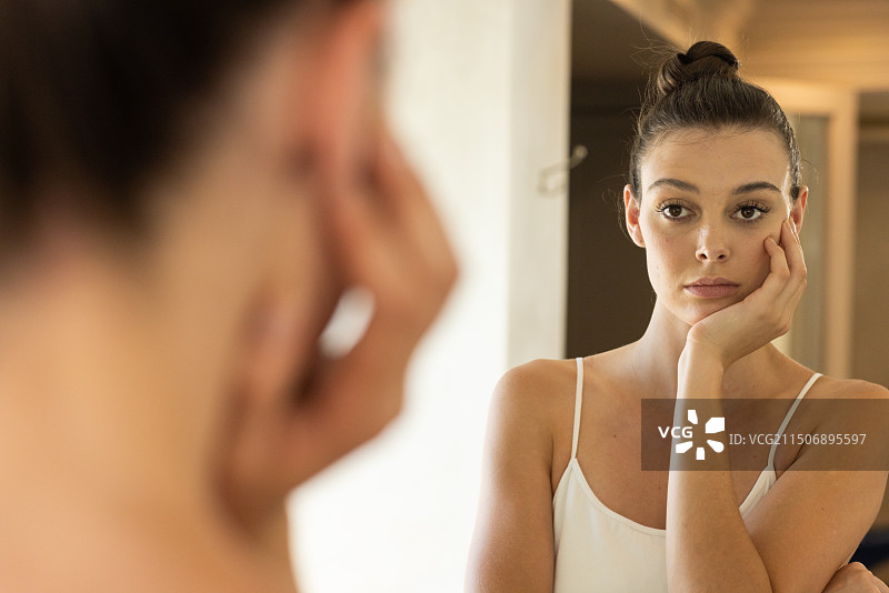 年轻女子手托下巴，看着镜子里的自己图片素材