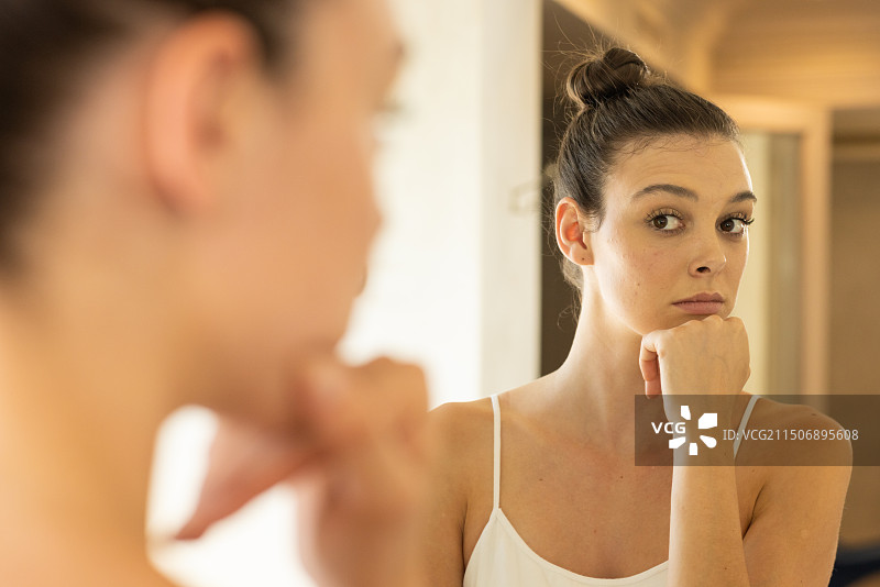照镜子：年轻女子在家中托着下巴沉思图片素材