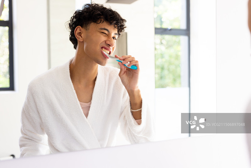 清晨，年轻男人在浴室里穿着浴袍照镜子刷牙图片素材