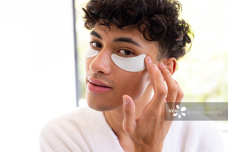 使用眼膜，年轻男人在家穿着浴袍享受护肤程序图片素材