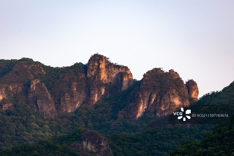 傍晚，夕阳的余晖下，连绵的山脉和山上的植被，以及被照亮的岩石山脊。图片素材