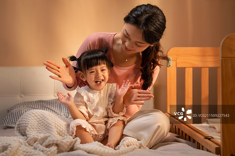 房间里年轻妈妈陪伴女儿在床上玩耍图片素材