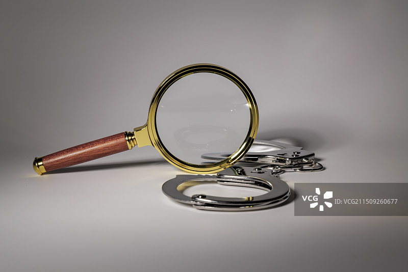 白色背景下的放大镜和手铐的特写镜头图片素材