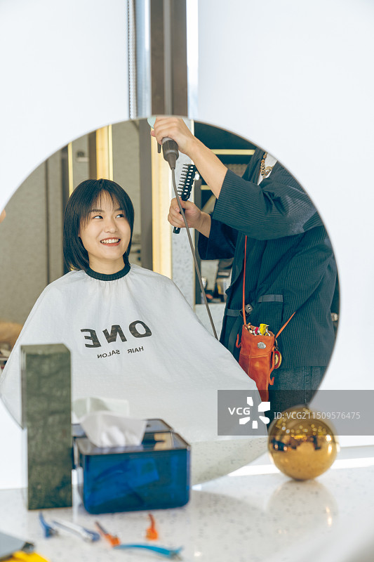 美发厅镜子里美发师给顾客做头发图片素材