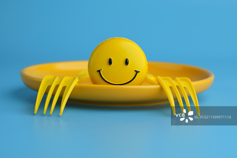 蓝色背景中黄色盘子中的笑脸和叉子抽象创意图图片素材