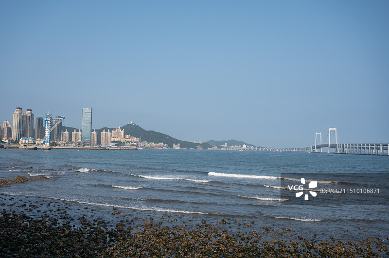 海边城市天际线风光，大连星海湾跨海大桥海上风光，层积海浪、礁石与大连星海湾大桥，夏日海浪海滩风光图片素材