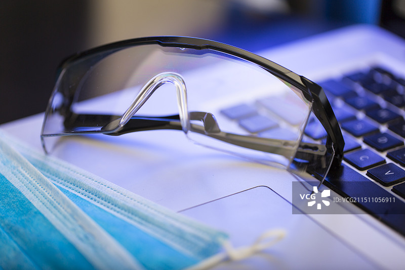 笔记本电脑、医用口罩和护目镜静物图片素材