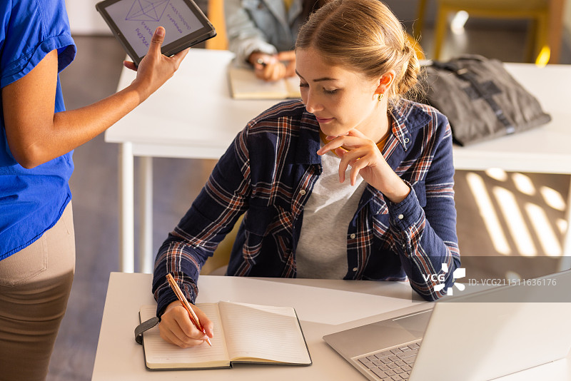 高中课堂上，少女在笔记本上写作并使用笔记本电脑图片素材