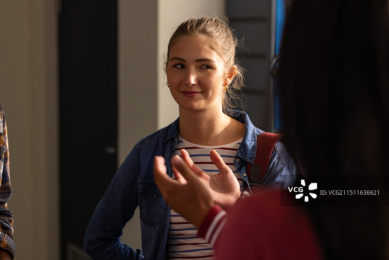 在高中走廊里，听朋友说话并微笑的少女图片素材