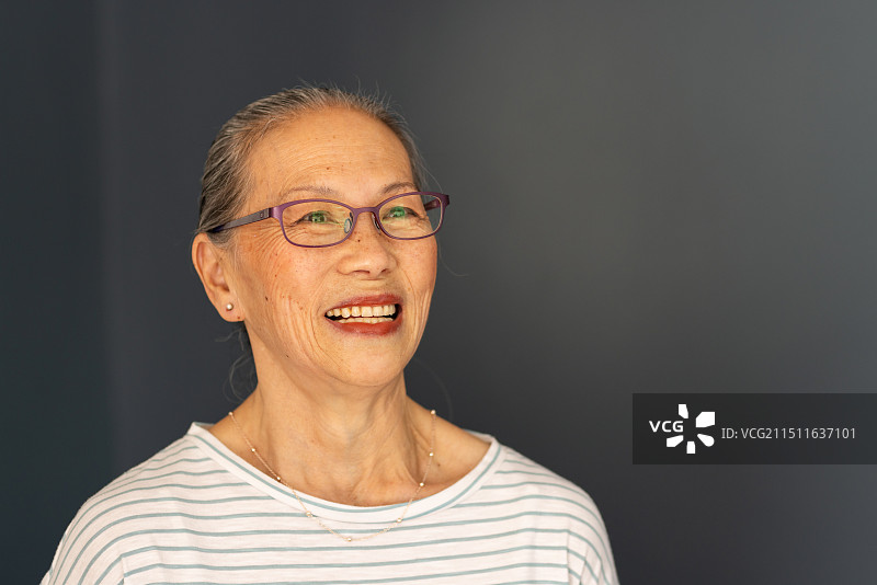 戴着眼镜、身穿条纹衬衫、面带笑容、抬头仰望的亚洲老年妇女图片素材