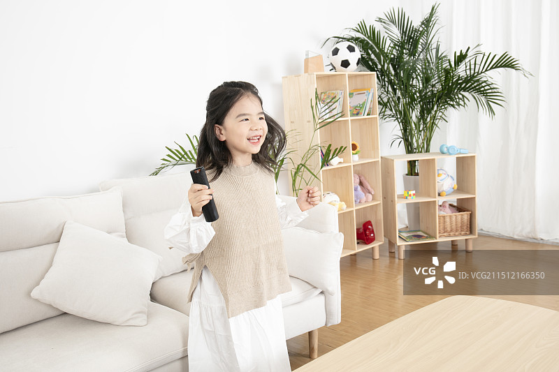 在客厅里手拿遥控器看电视的小女孩图片素材