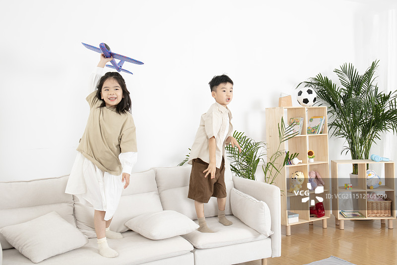 站在客厅沙发上玩飞机模型的两个小朋友图片素材