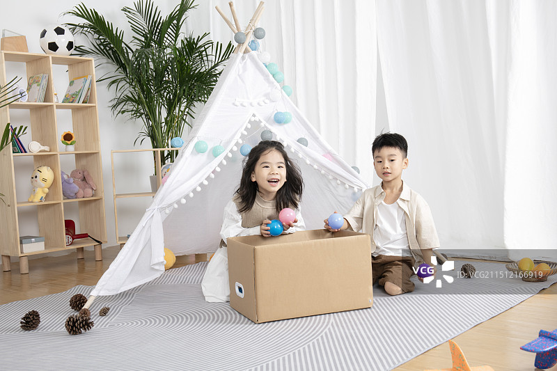 在儿童帐篷前玩纸箱子游戏的两个小朋友图片素材