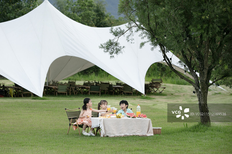 坐在户外天幕前吃水果的三个小朋友图片素材