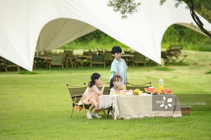 坐在户外天幕前吃水果的三个小朋友图片素材