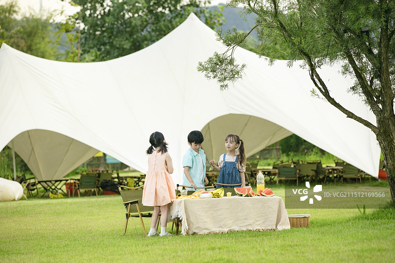 坐在户外天幕前吃水果的三个小朋友图片素材