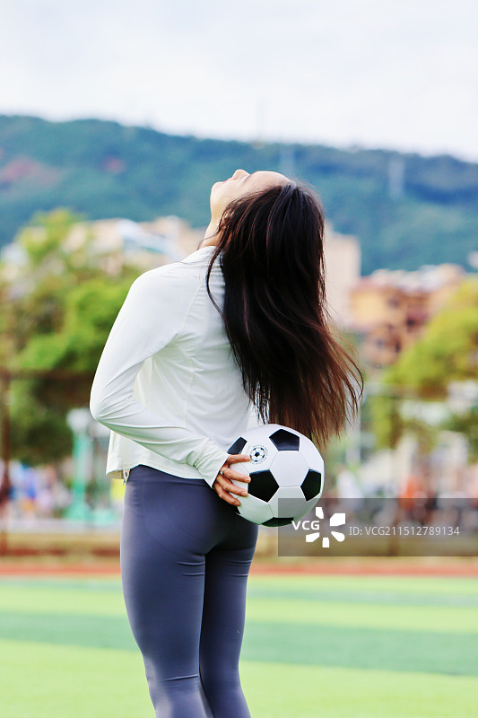 女生在草地上踢足球的后视图图片素材