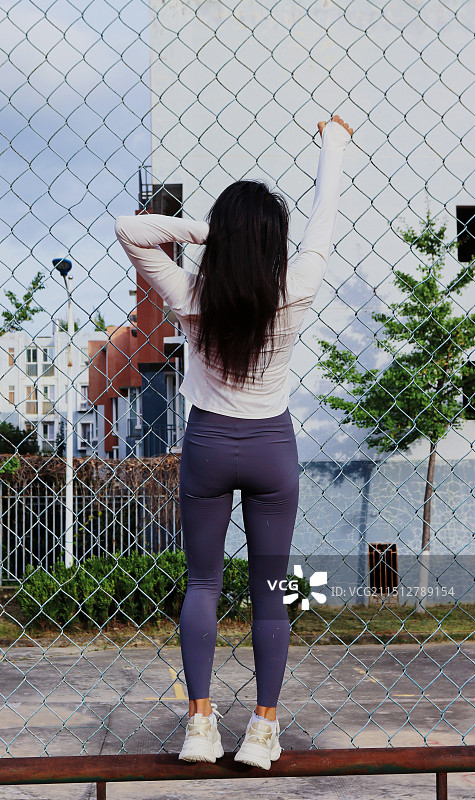 站在铁丝网围栏上的美女的后视图图片素材