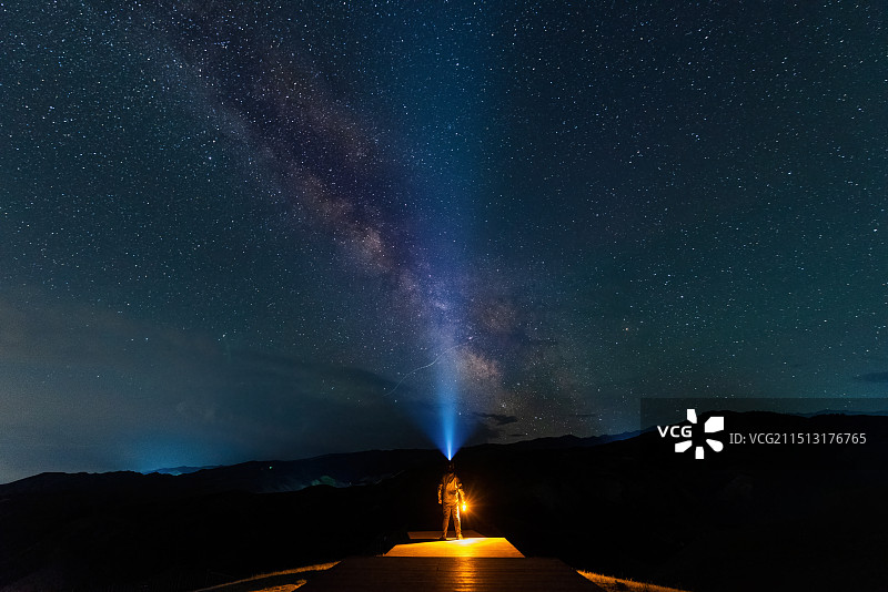 中国新疆伊犁草原男青年手持露营灯佩戴强光头灯在银河星空下照明镜头特写图片素材