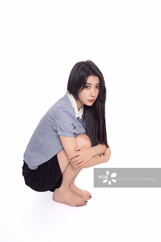 白背景前蹲在地上的年轻东方少女图片素材