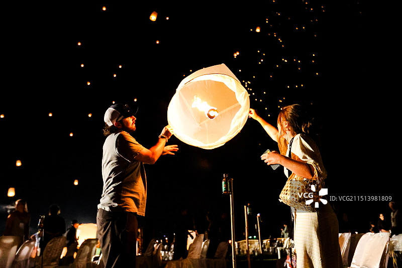 两人在夜晚的天灯节放飞孔明灯，天空中布满了星星点点的灯光，场面浪漫温馨图片素材
